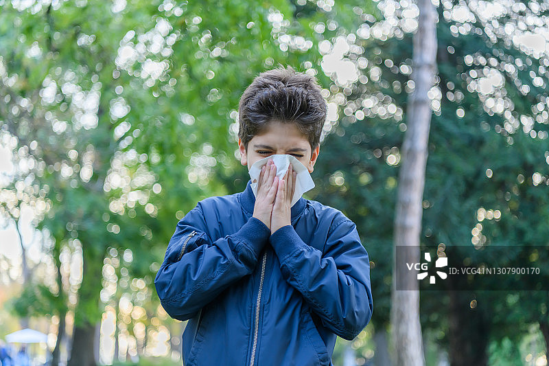 患流感的小男孩在公园里散步，用纸巾打喷嚏。图片素材