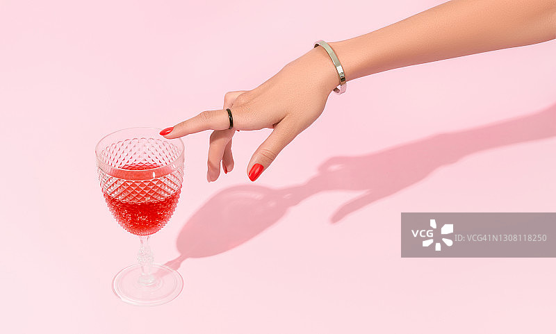 女士用手触摸粉红色背景上的玻璃。修指甲的设计趋势图片素材