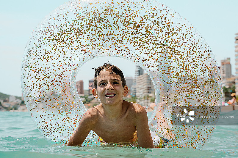 在贝尼多姆的夏天，快乐的白人孩子看着镜头享受浮动或内胎沐浴图片素材