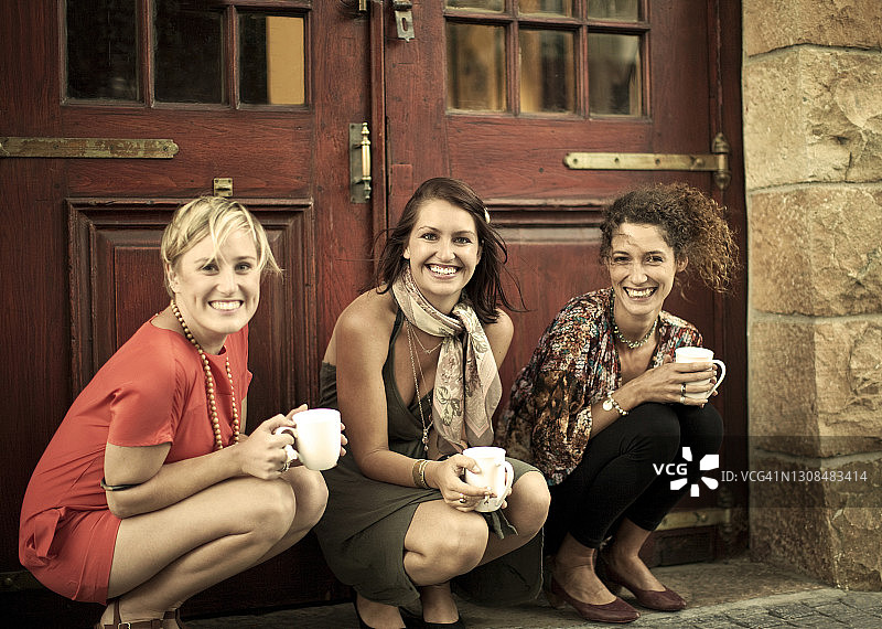 年轻的女人拿着咖啡杯微笑着蹲在门边图片素材