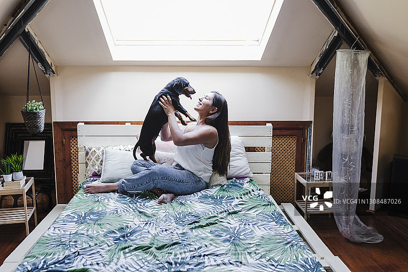 爱玩的女人坐在家里的床上抱着狗图片素材