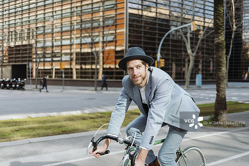 商人戴着帽子在城市里骑自行车图片素材
