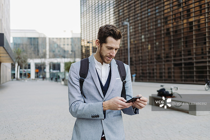 商人背包使用智能手机在城市图片素材