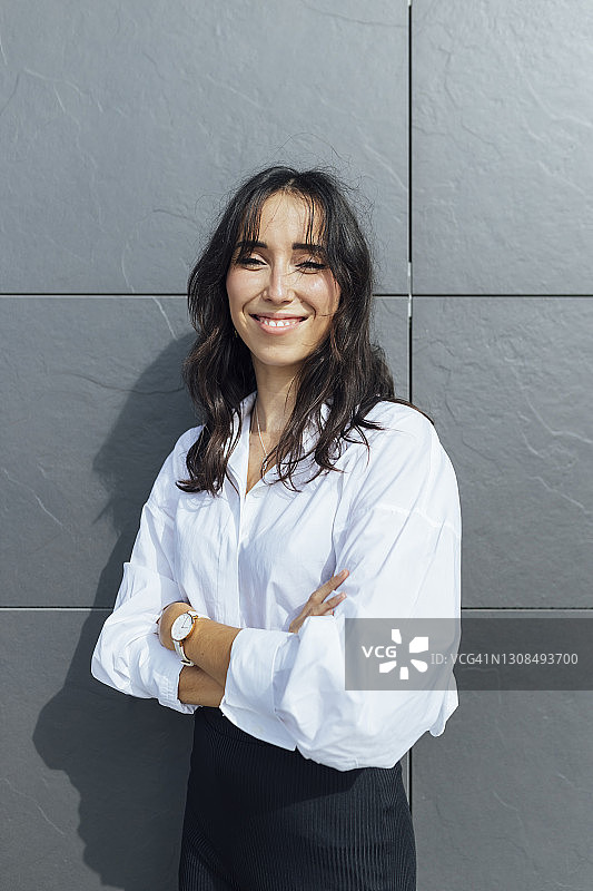 微笑的女企业家双臂交叉，站在灰色的墙壁图片素材