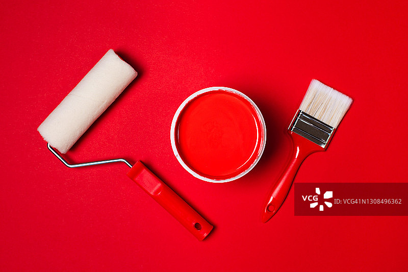 鲜红色颜料桶旁边的滚筒和油漆刷与红色手柄在充满活力的红色背景。平的风格。为您的设计复制空间。家居室内重新装修的概念。颜色样本的设计理念图片素材