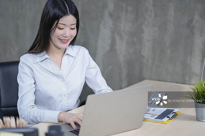 快乐的年轻亚洲女性在现代办公室工作图片素材