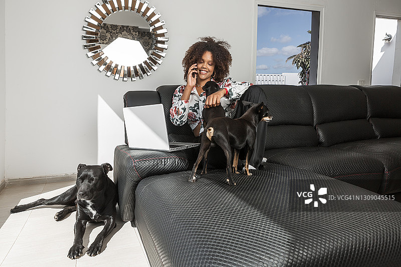 一名黑人女性在有狗的房间里用智能手机说话图片素材