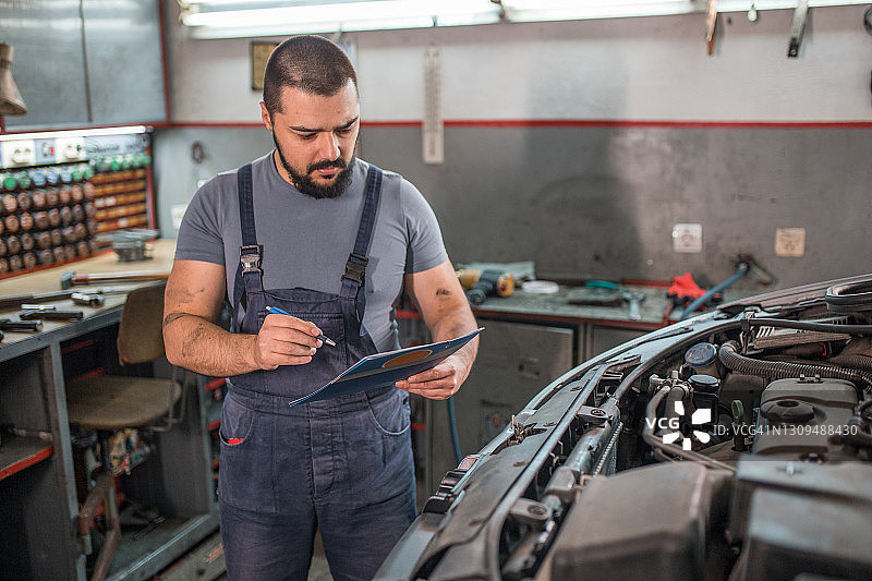 汽车修理工在汽车修理厂用夹板检查发动机图片素材