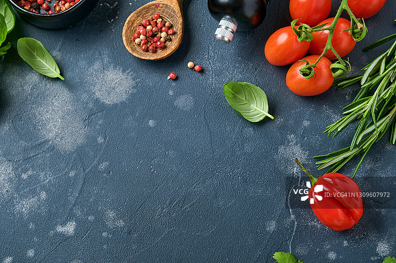 食物烹饪的背景。新鲜迷迭香，香菜，罗勒，樱桃番茄，辣椒，橄榄油，香料香草和蔬菜在黑色石板桌上。食物配料俯视图。图片素材