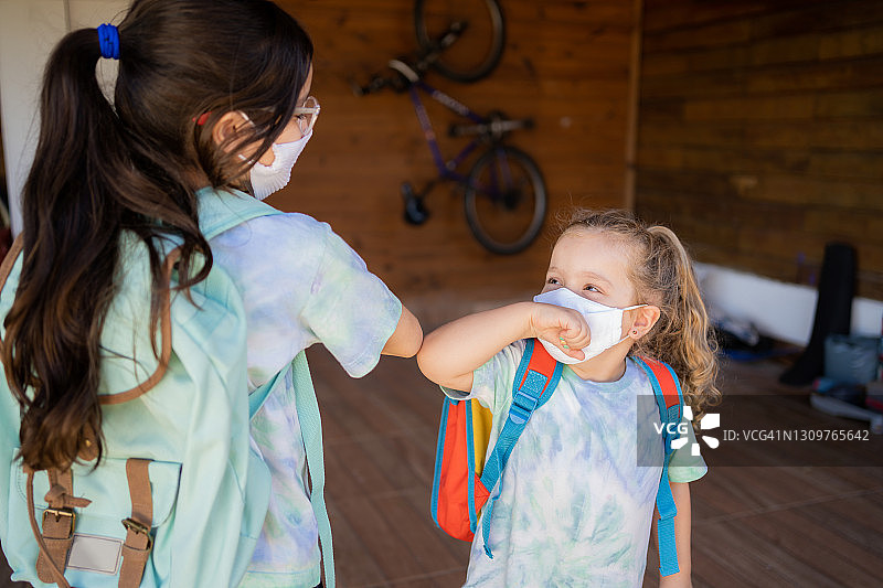 2019冠状病毒病期间，姐妹们戴着防护口罩准备上学。新常态图片素材