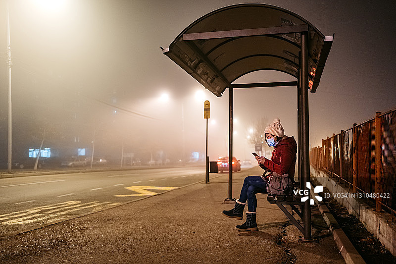 一个戴口罩的女人在公交站用手机图片素材