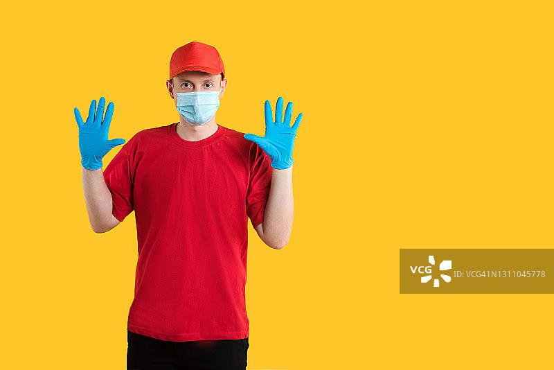 身穿红色制服，黄色背景上戴着面具和手套的快递员。副本的空间。工作室。交付的概念图片素材