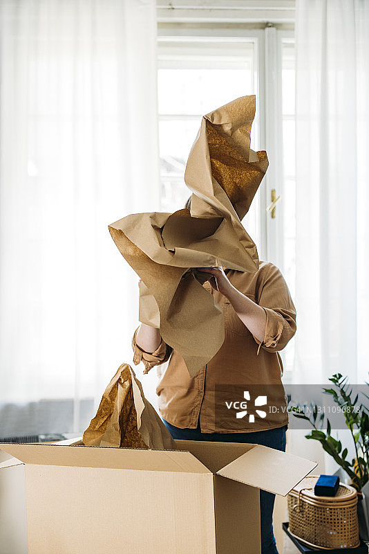 匿名的大码女人用包装纸遮住脸，站在窗前图片素材