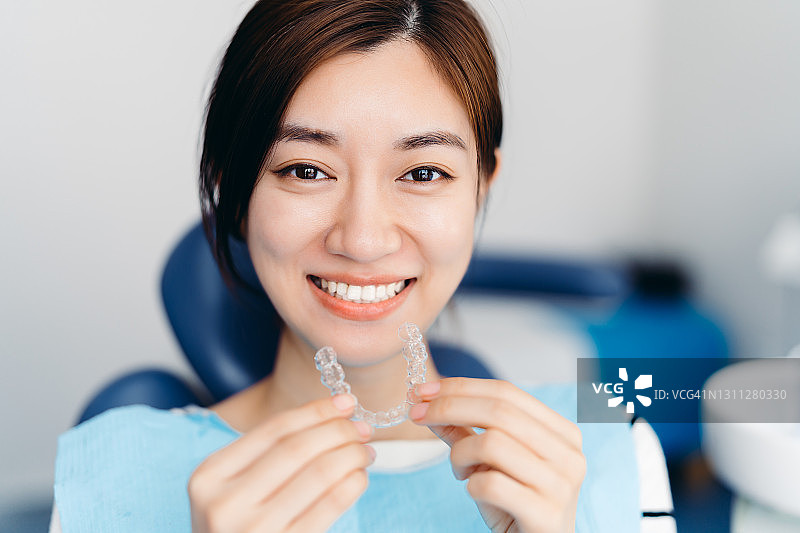 亚洲年轻迷人的女人在牙科诊所拿着正畸固位器。Invisalign正畸治疗的概念。图片素材