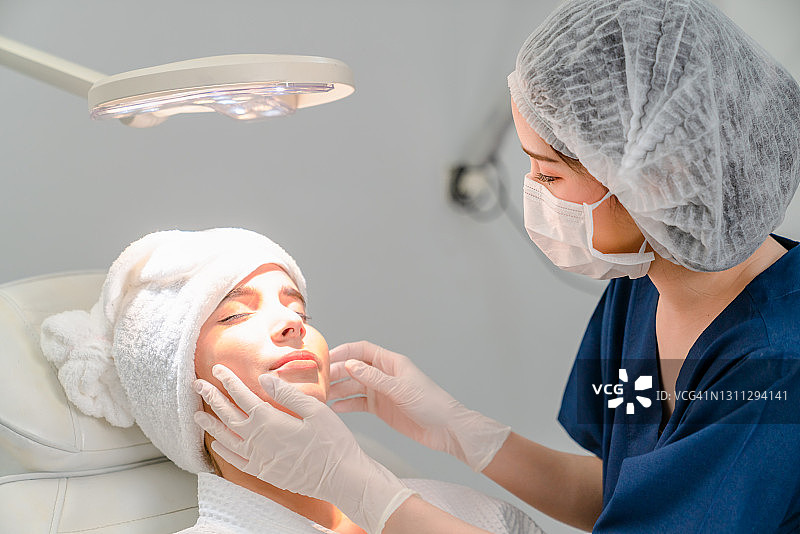 年轻的女医生与美丽的女人在美容诊所的背景接受面部微晶磨皮治疗。图片素材