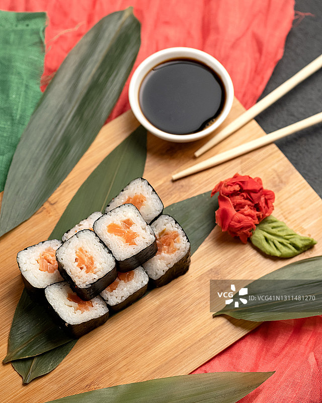 漂亮的寿司卷。米饭，三文鱼和海苔放在砧板上，配上酱油，芥末，生姜和筷子。传统的东方美食。高角度视图图片素材