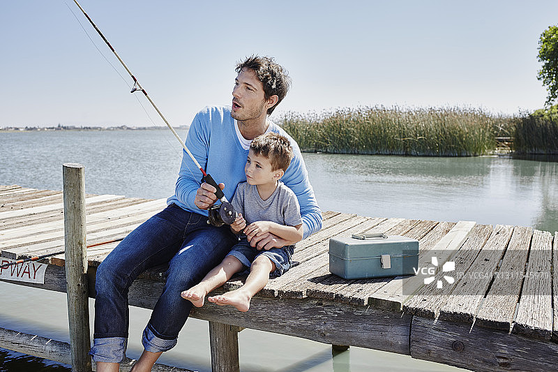 一个成熟的男人和一个小男孩坐在码头上一起钓鱼图片素材