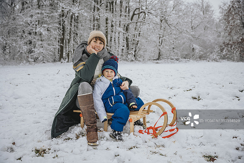 冬天，母子俩坐在雪地上的雪橇上图片素材