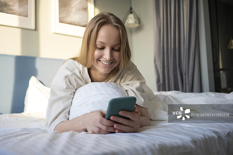 微笑的女人躺在床上使用手机图片素材