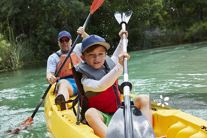 假期里可爱的男孩和父亲在湖中划独木舟图片素材