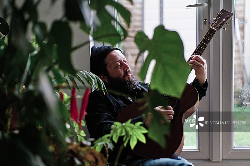 一个成年人在家靠窗弹吉他图片素材