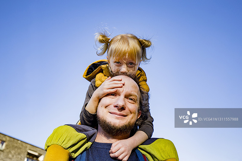 微笑的男人背着金发的女儿背对天空图片素材