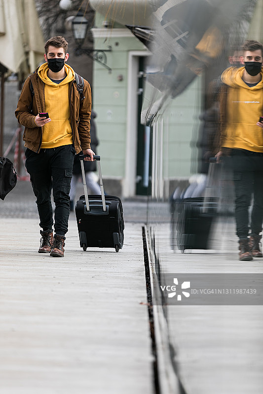 游客戴着医用口罩，提着旅行箱走在城市街道上图片素材