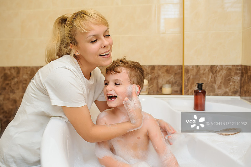 男孩在浴缸里和他的妈妈一起洗和玩泡沫和肥皂泡图片素材
