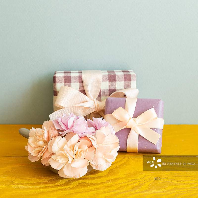 木桌上放着康乃馨花的礼盒。蓝色背景图片素材