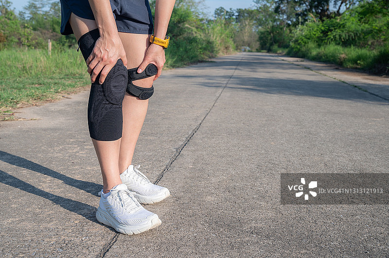 跑步的女人抱着她的膝盖，当她遭受膝盖疼痛时，她戴着膝盖支架作为支撑，当你有膝盖疼痛时。图片素材