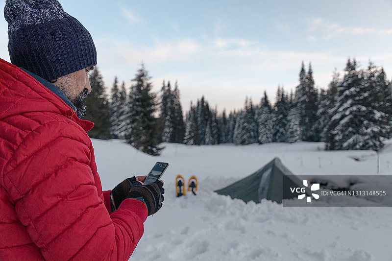 游客在冬季山地露营时在帐篷附近使用手机。在2019冠状病毒病大流行期间，自然是孤独的。心理健康和生活平衡。图片素材