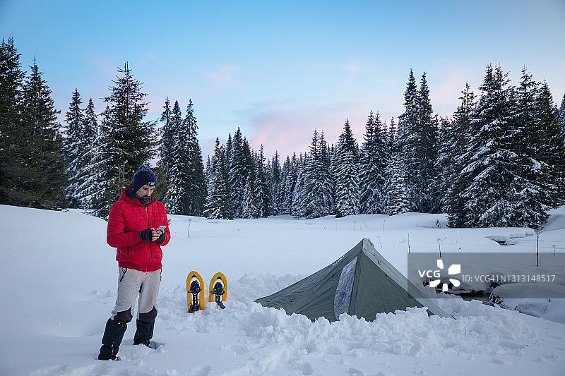 游客在冬季山地露营时在帐篷附近使用手机。在2019冠状病毒病大流行期间，自然是孤独的。心理健康和生活平衡。图片素材