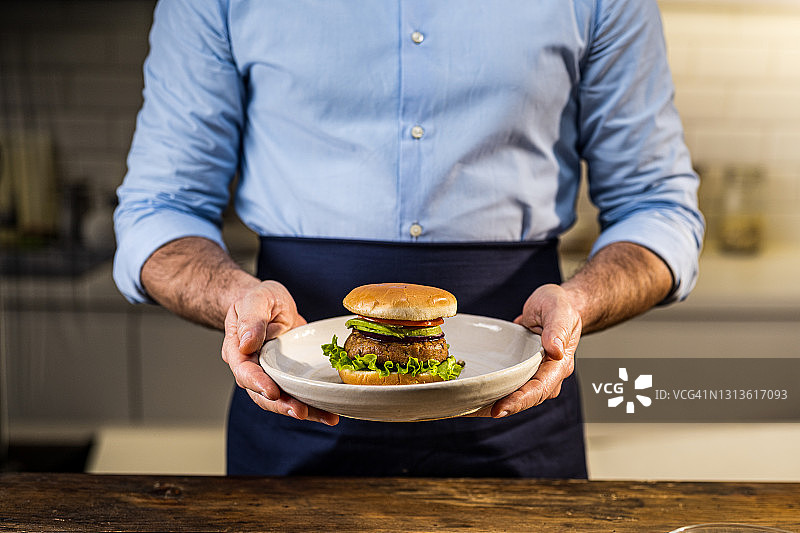一个男人拿着盛在盘子里的素食汉堡图片素材