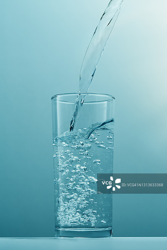 从瓶子中倒入干净的饮用水到透明的玻璃中，并产生气泡图片素材