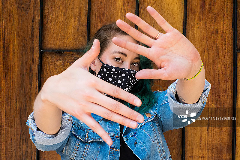 年轻女子绿色头发戴着面具和手指框架在墨西哥城，木制背景图片素材