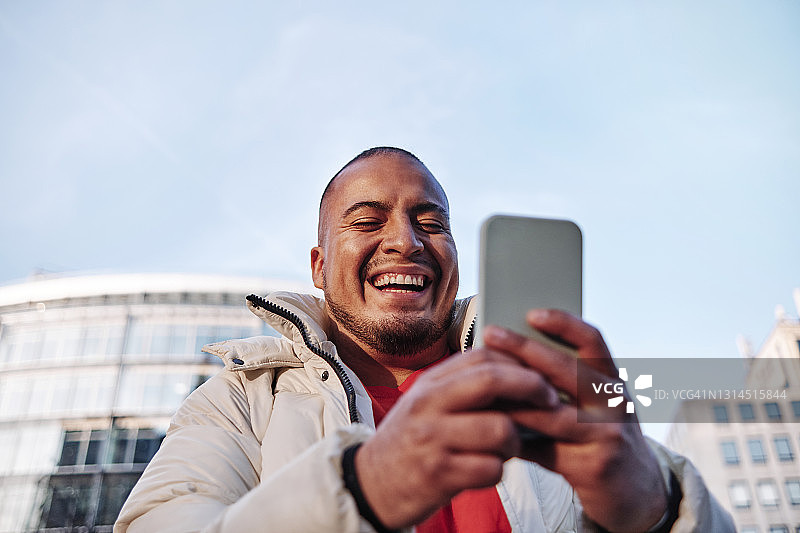 一个在阳光明媚的日子里使用智能手机的快乐男人图片素材