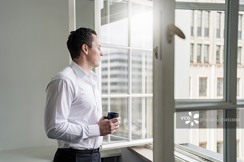 男企业家拿着咖啡杯，看着窗外的工作场所图片素材