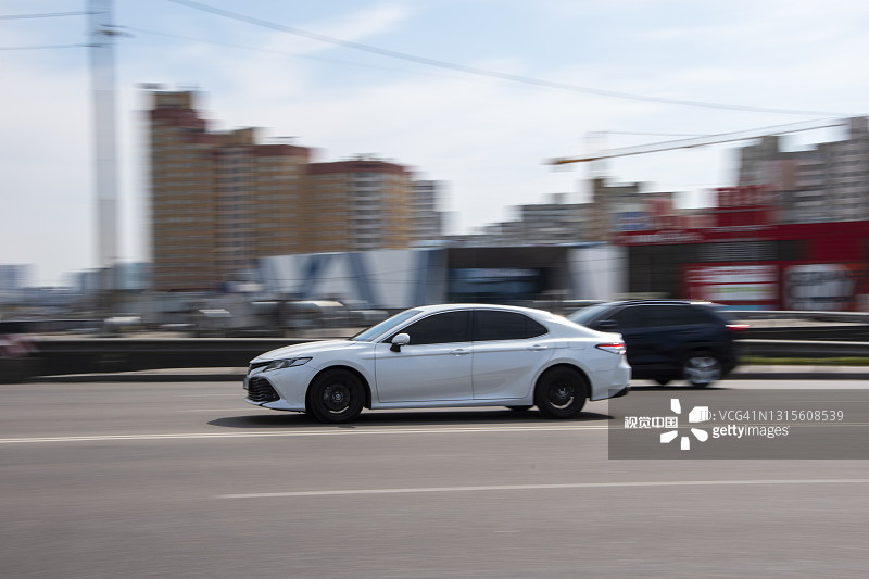 白色丰田凯美瑞车在街上行驶。图片素材