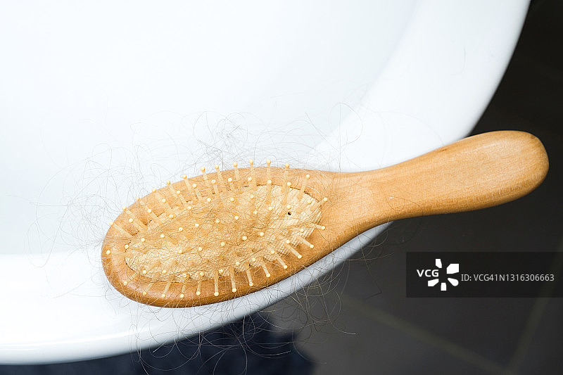 落在木梳上的女性头发，放在浴缸或水槽的边缘。头部健康问题的概念，由于压力和抑郁造成的身体缺陷，癌症化疗和放射治疗的后果。图片素材