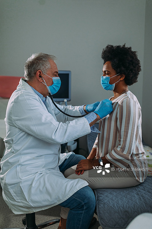 在医院检查时戴口罩的资深医生及其病人图片素材