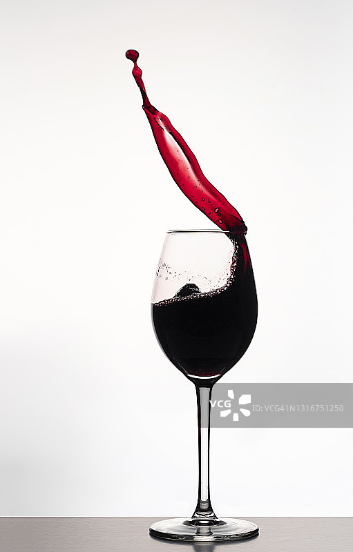 在白色的背景下，一杯红酒的水滴和飞溅。图片素材