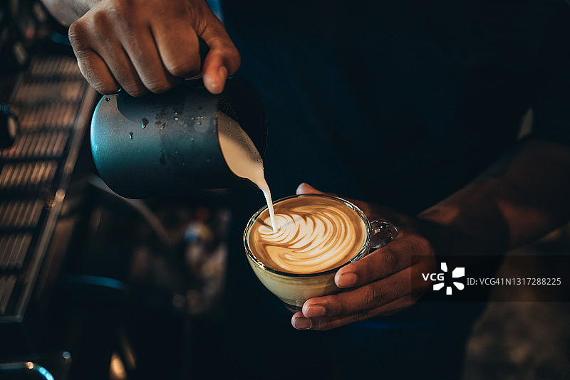 近距离的咖啡师的手制作一杯咖啡和如何使拿铁艺术的咖啡师专注在牛奶和咖啡在咖啡馆图片素材