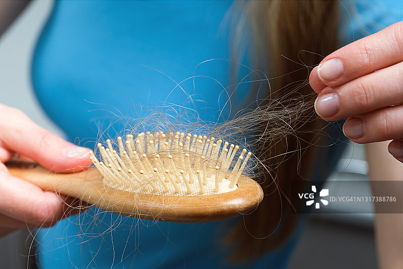 一位妇女手里拿着一把木梳子，梳理完掉下来的头发后把它清理干净。头部健康问题的概念，由于压力和抑郁造成的身体缺陷，癌症化疗和放射治疗的后果。图片素材