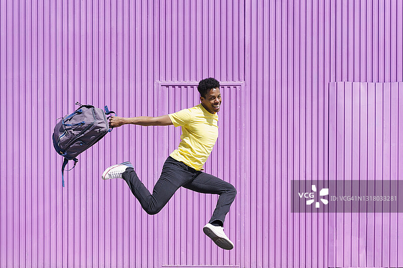 快乐的男人背着背包在紫色小屋旁跳跃图片素材