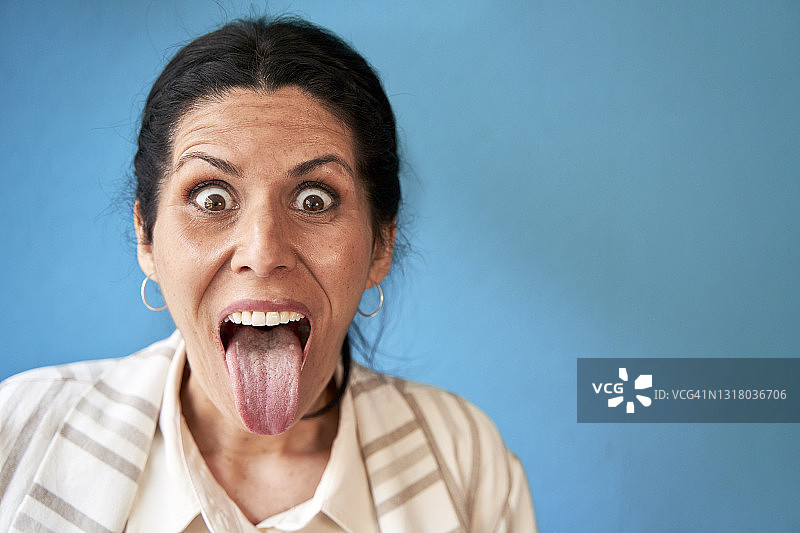 成熟的女人在蓝墙前吐舌头图片素材
