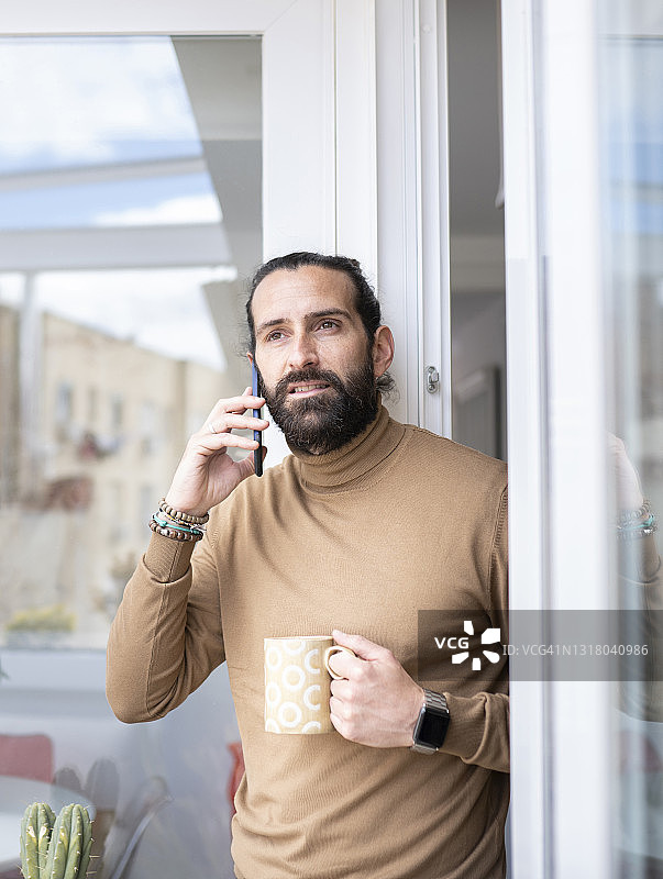 一个成熟的男人在门口一边拿着杯子一边讲智能手机图片素材