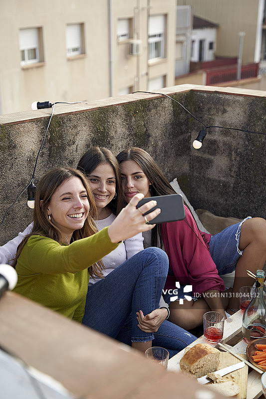 微笑的女性朋友在屋顶上用智能手机自拍图片素材