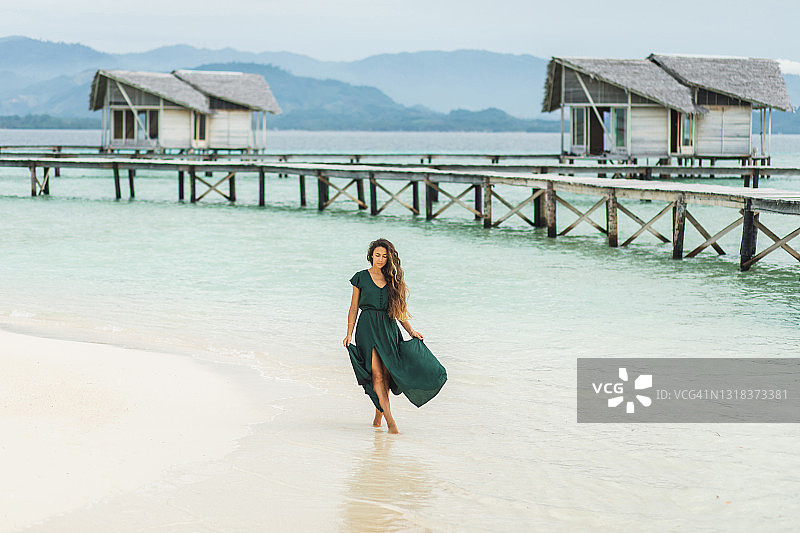 身穿绿色夏装的女子走过马尔代夫豪华酒店的白色沙滩图片素材