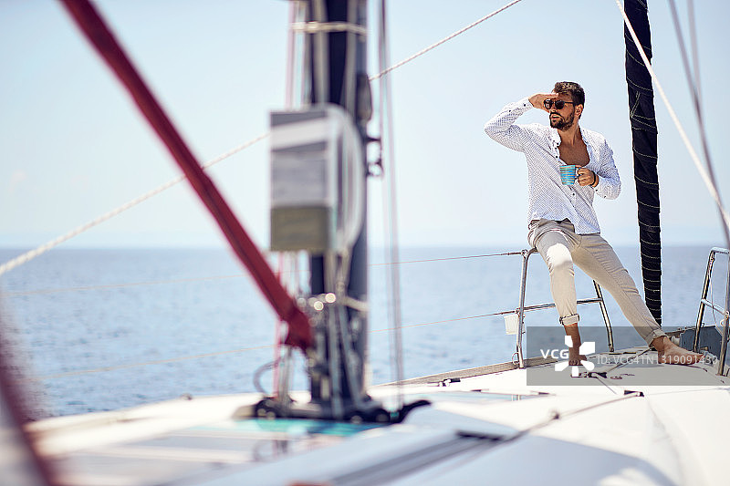 一个年轻英俊的男模特正在海边的游艇上享受风景和咖啡拍摄照片。夏天,大海,假期图片素材
