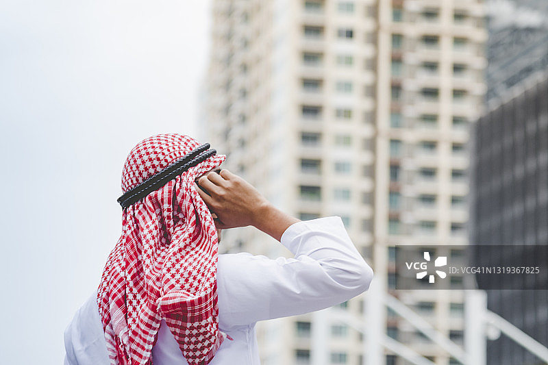 伊斯兰男子使用智能手机应用程序组织日程议程，重点在手握智能手机穆斯林现代阿联酋城市。阿拉伯男人戴着头巾和穆斯林正式服装在网上发送短信图片素材